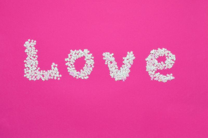 Letters from holographic confetti forming word LOVE written on pink background. Valentines Day, wedding, bachelorette celebration concept.