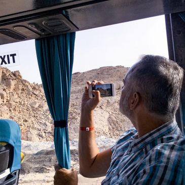 A man takes a photo of rocky mountains from a bus window.
