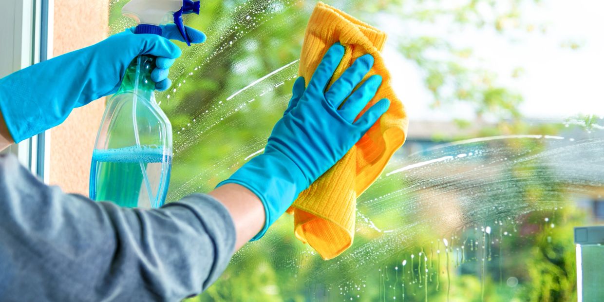 Person cleaning a window with gloves, spray bottle, and cloth.