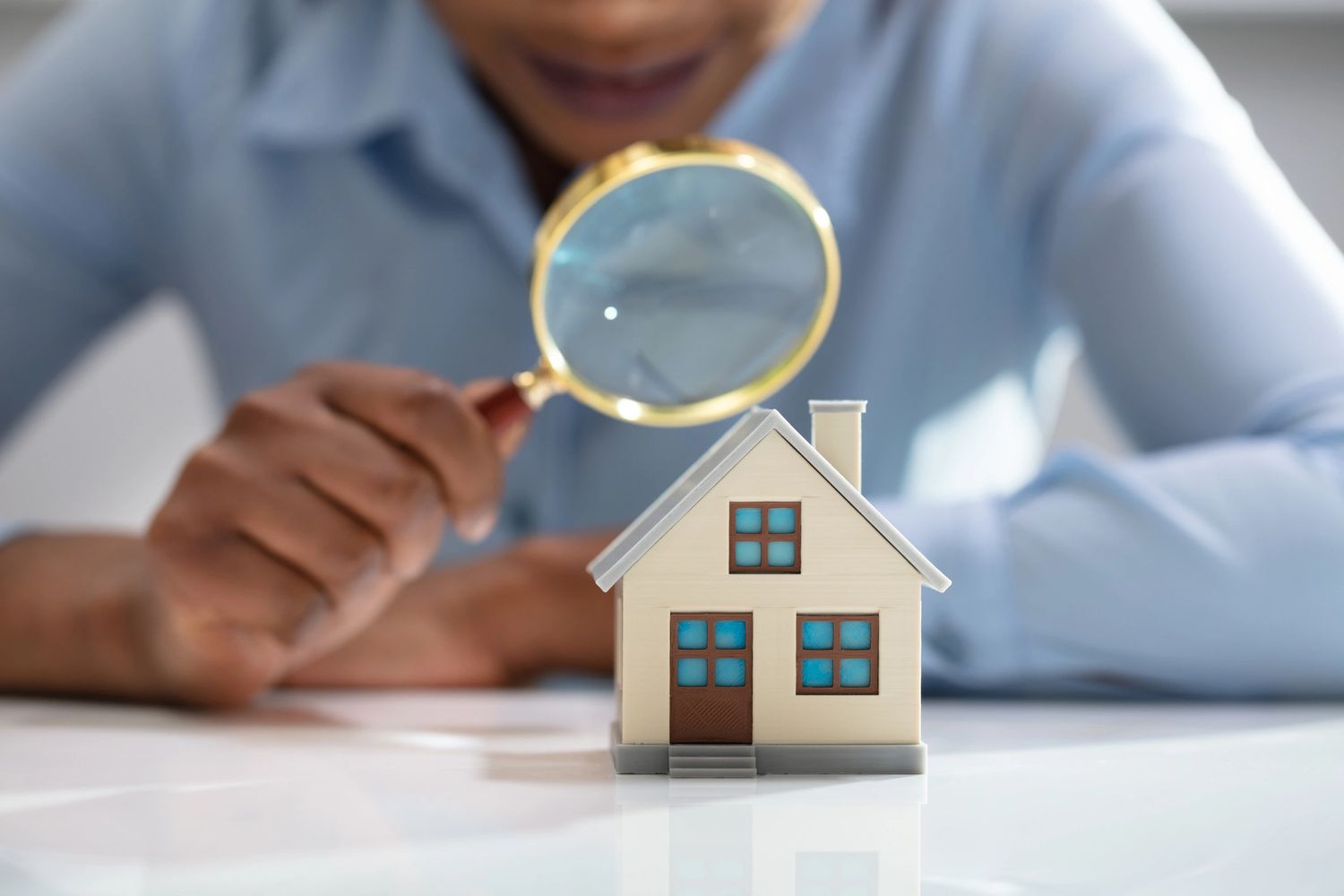 Person examining a miniature house with a magnifying glass.