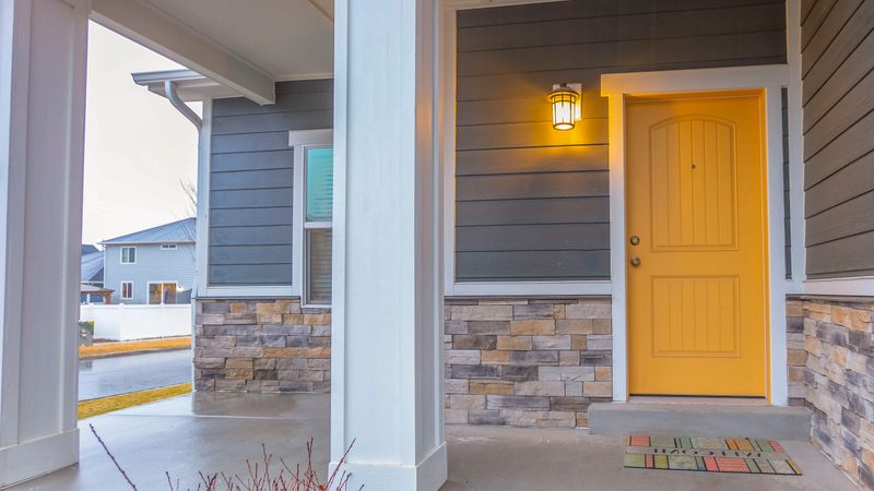 Panorama Entryway of a home with stairs going up to the front porch and door. Rectangular pillars, stone brick wall, and horizontal siding defines the facade of this home.