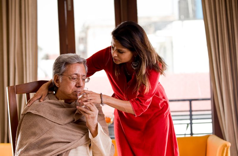 Woman giving water to her ailing father at home
