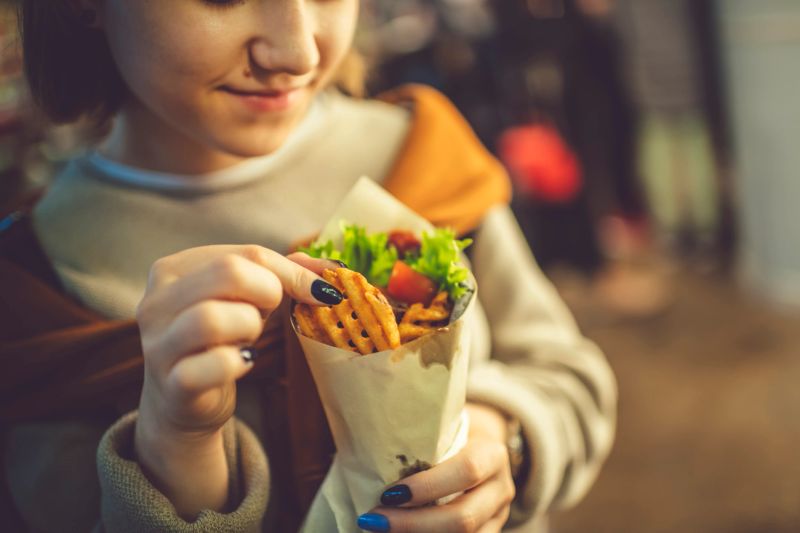 Cute teenage girl eating kebab, shwarma  or roll outdoors