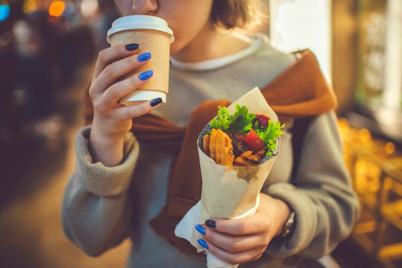 Cute teenage girl enjoying tea and kebab, shwarma or roll outdoors