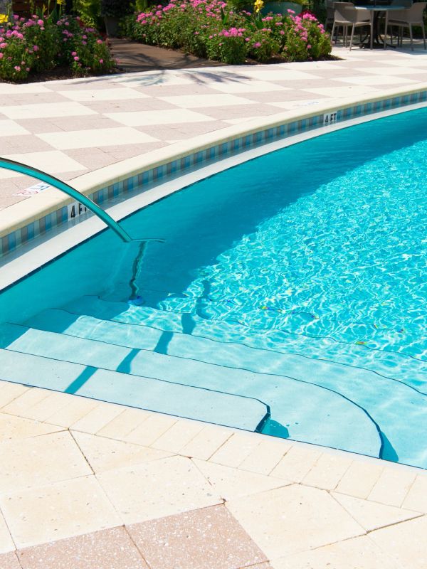 Clear blue pool water with steps and surrounding flowers.