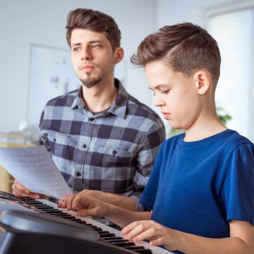 A man teaches a boy to play the piano using sheet music.