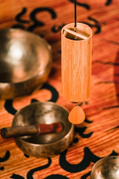 Hand holding a wooden wind chime over a patterned surface with Tibetan singing bowls nearby.