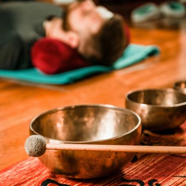 Person lying down near Tibetan singing bowls with mallet.