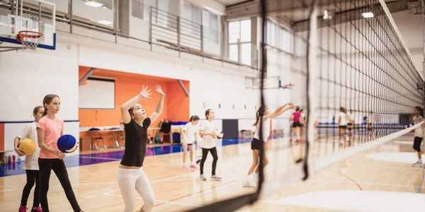 Girls playing volleyball in a gymnasium during practice.