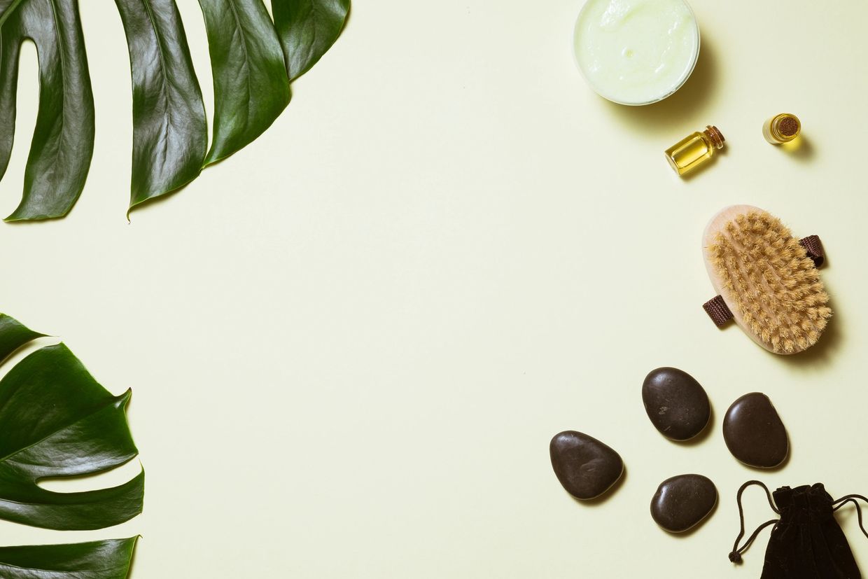 Spa essentials with green leaves and massage stones on a light background.