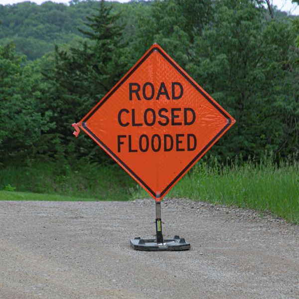 Orange road sign warning of road closure due to flooding.