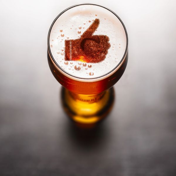 A glass of beer with a thumbs-up foam design on top.