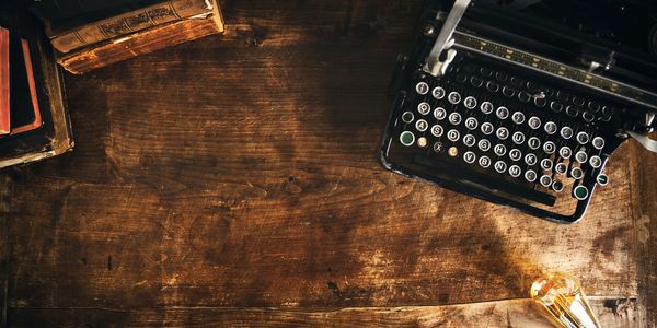 Vintage typewriter, old books, and a clock on a wooden desk.