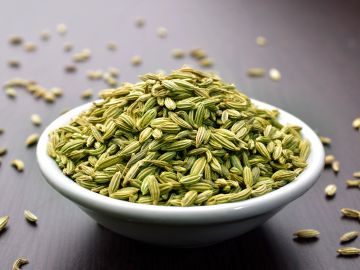 A bowl of fennel seeds on a wooden surface.