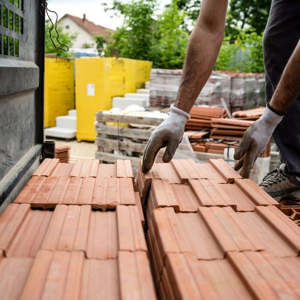 Worker unloading terracotta roof tiles from a truck at a construction site.