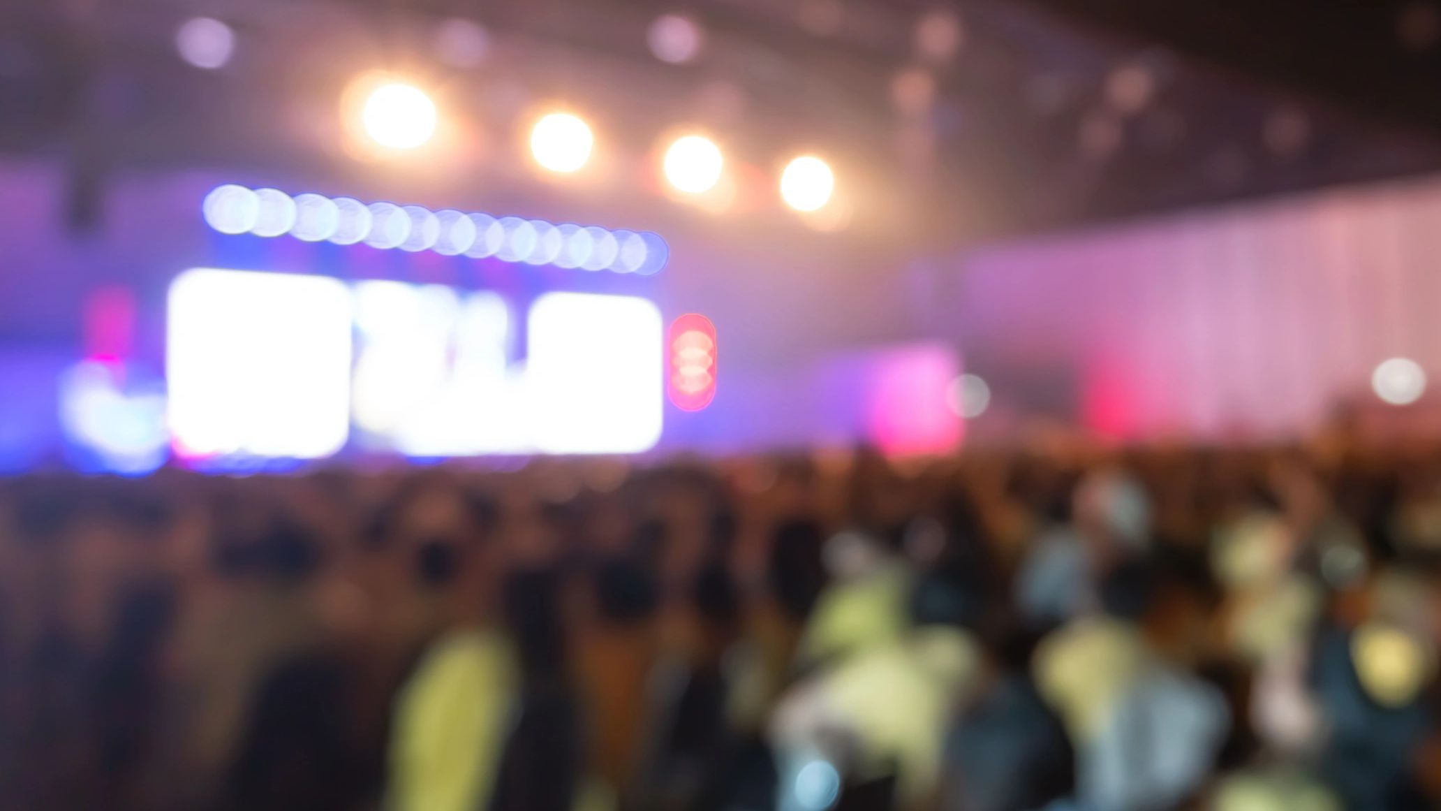 Blurred image of a crowded indoor event with bright stage lights.
