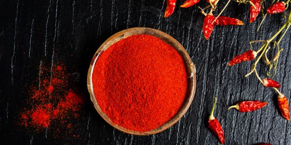 Bowl of red chili powder with dried red chilies on the side.