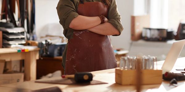 Confident woman artisan in a workshop wearing a leather apron.