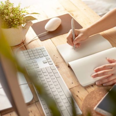 Person writing in a notebook near a keyboard and mouse on a wooden desk.