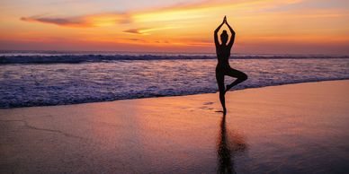 Person practicing yoga on the beach at sunset.