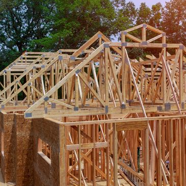 Wooden frame structure of a house under construction with trees in background.
