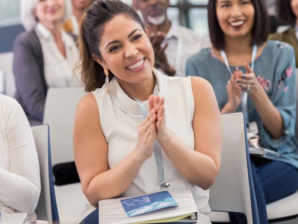 A woman smiling and clapping during a seminar or meeting.