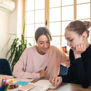 Two women studying together at a table in a bright room.