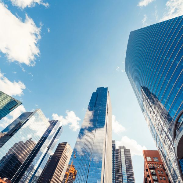 Skyscrapers reflecting clouds against a bright blue sky in a city.