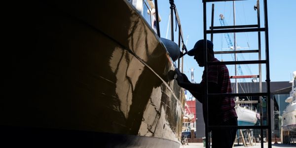 Silhouette of a man painting a boat hull at the dock.
