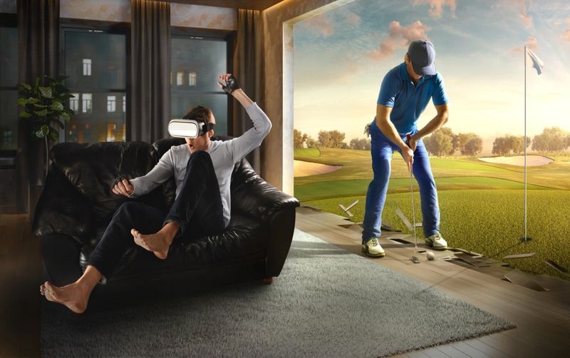 Young man at home on a black sofa with VR headset emotionally playing in virtual reality Golf