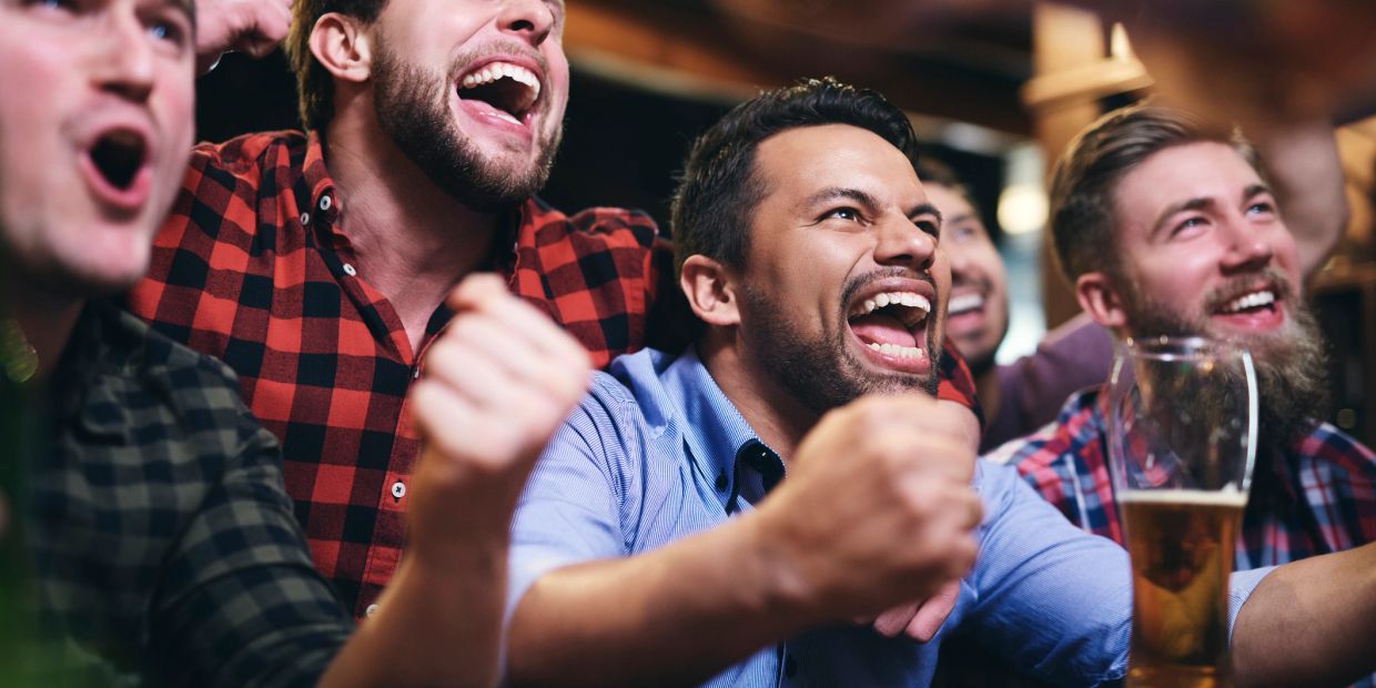 Group of men cheering excitedly with drinks.