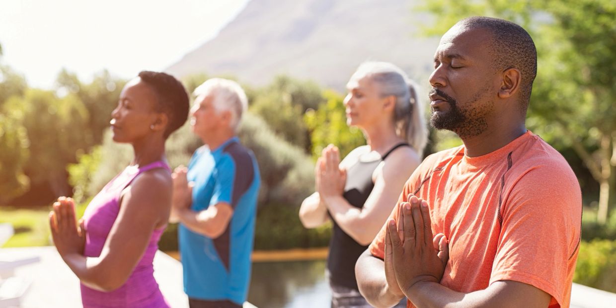 Group meditating outside with hands in prayer position.