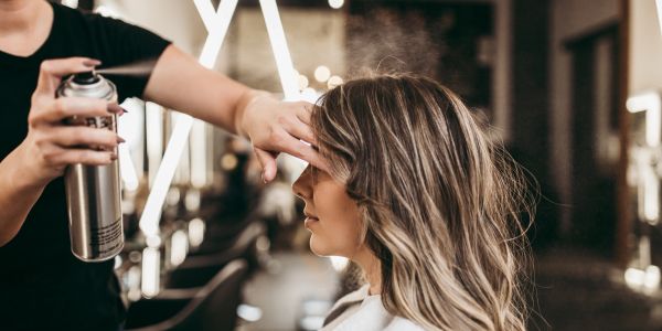 Stylist applying hairspray to woman's hair.