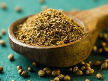 Ground coriander in a wooden spoon with whole coriander seeds scattered.