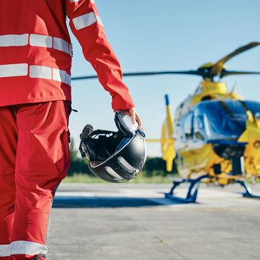 Rescue worker in red uniform holding a helmet near a yellow helicopter.