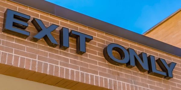 Black EXIT ONLY sign on a brick building under clear blue sky.