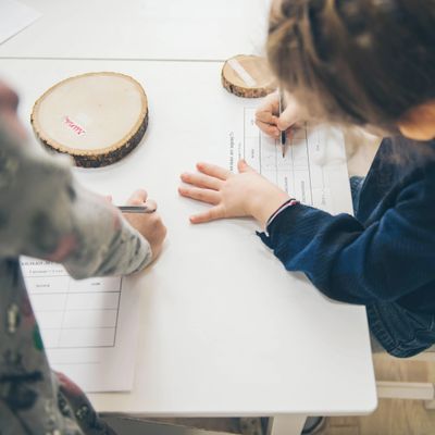 Children writing on papers at a table with wood slices.