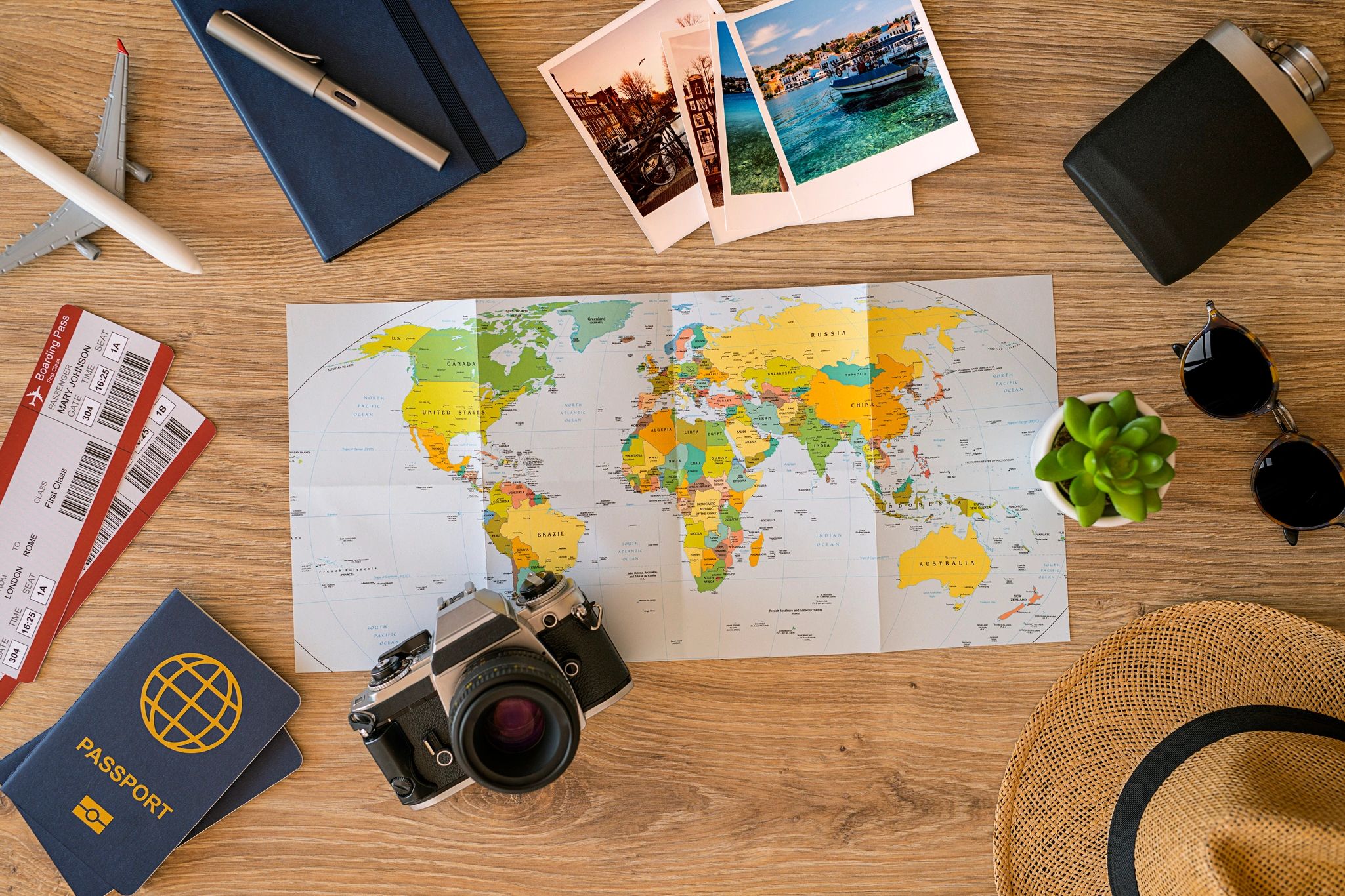 Image shows a map, camera, passport, tickets, pictures, drink container, sunglasses, small potted pl