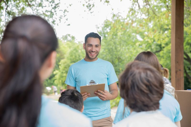 Happy young Hispanic man leading a group of community volunteers in matching t-shirts