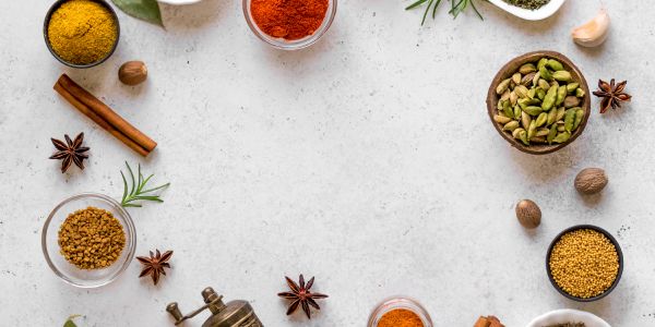 Various spices and herbs arranged around a white surface.