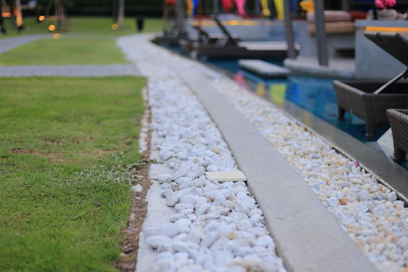 swimming pool drainage system grating covered with round white river stone pebble. swimming pool architectural detail design. White pebble contrasting with dark grey aggregate stone pool edge