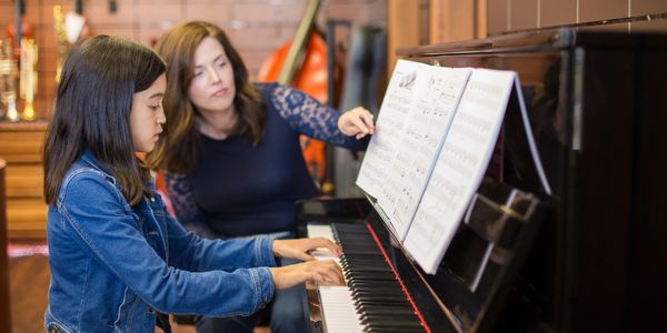 A young girl learns piano with a teacher pointing at sheet music.