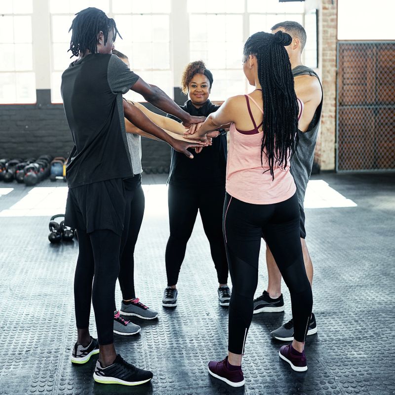 Shot of a cheerful young group of people forming a huddle together while one looks at the camera before a workout session in a gym