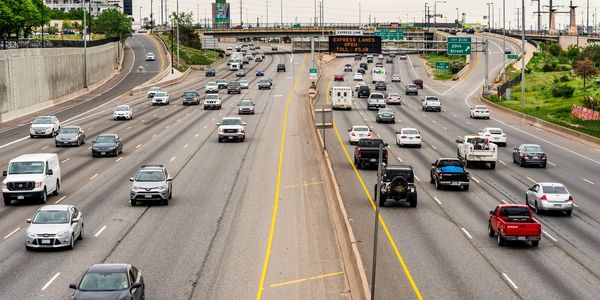 Busy multi-lane highway with cars and trucks under an overcast sky.