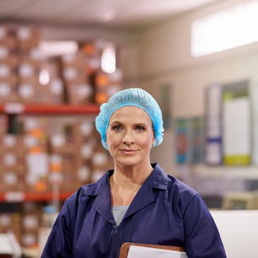 Woman in protective clothing and hairnet in a warehouse.