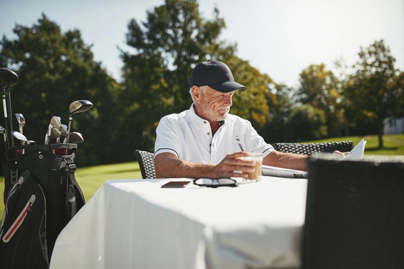 Smiling senior man reading a newspaper and drinking a coffee while relaxing at a course restaurant after a round of golf