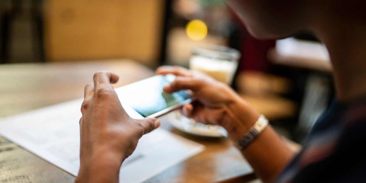 Person using a smartphone at a wooden table with a drink.
