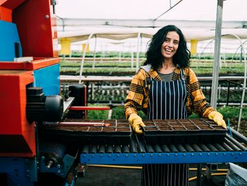 mujer agropecuaria con bandejas de posturas en la mano saliendo de una maquina expendedora