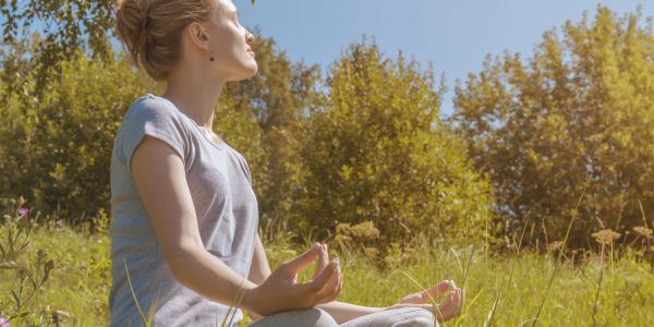 Woman meditating outdoors in a sunlit grassy field.