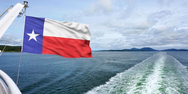 Texas flag waving on a boat over open water with islands in the distance.
